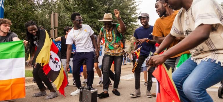 International students, some adorned with their countries flags, stop and dance while marching in the homecoming parade.