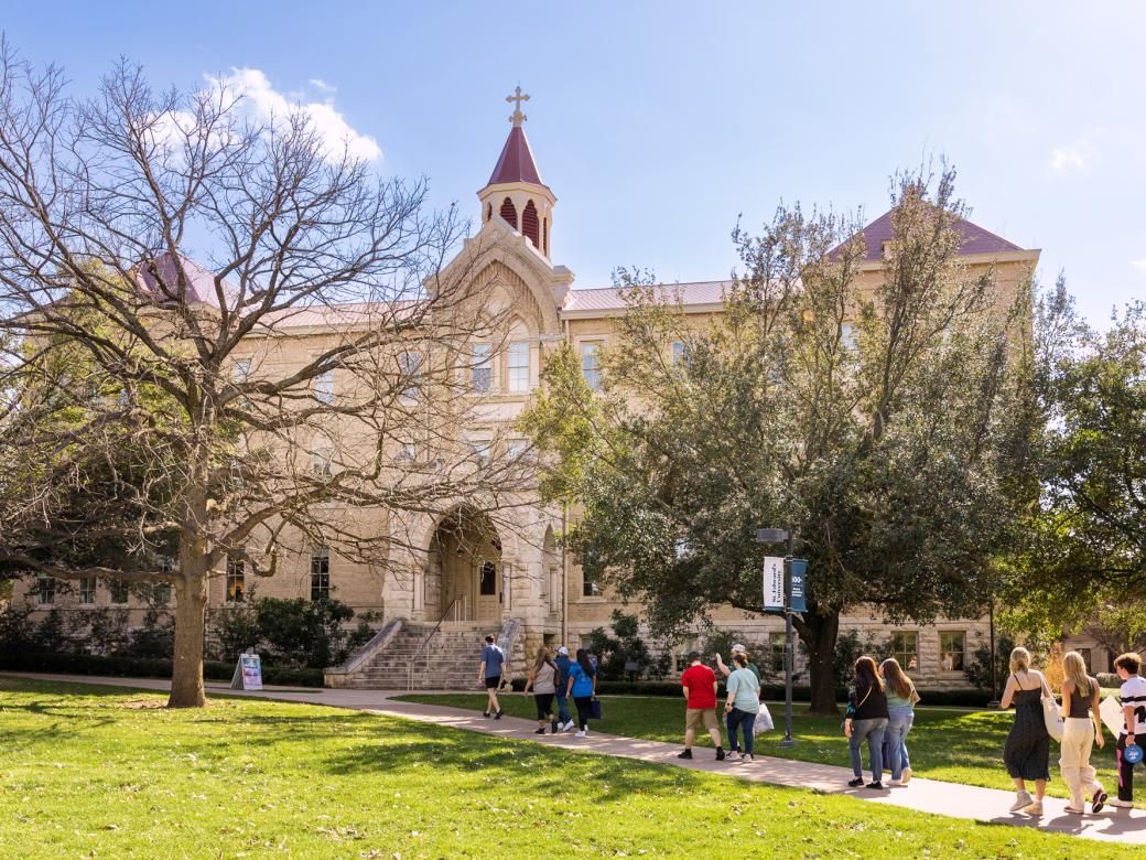 A group of people walk on a pathway in front of Holy Cross Hall.