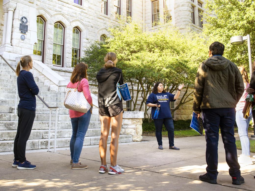 Prospective students and families stand near the steps of Main Building and listen to a student tour guide speak.