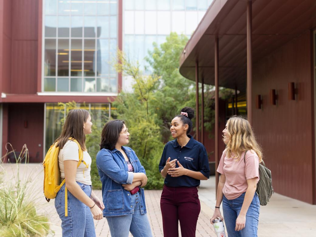 Three students stand around a student tour guide and listen as she speaks outside of John Brooks Williams Natural Sciences Center - South