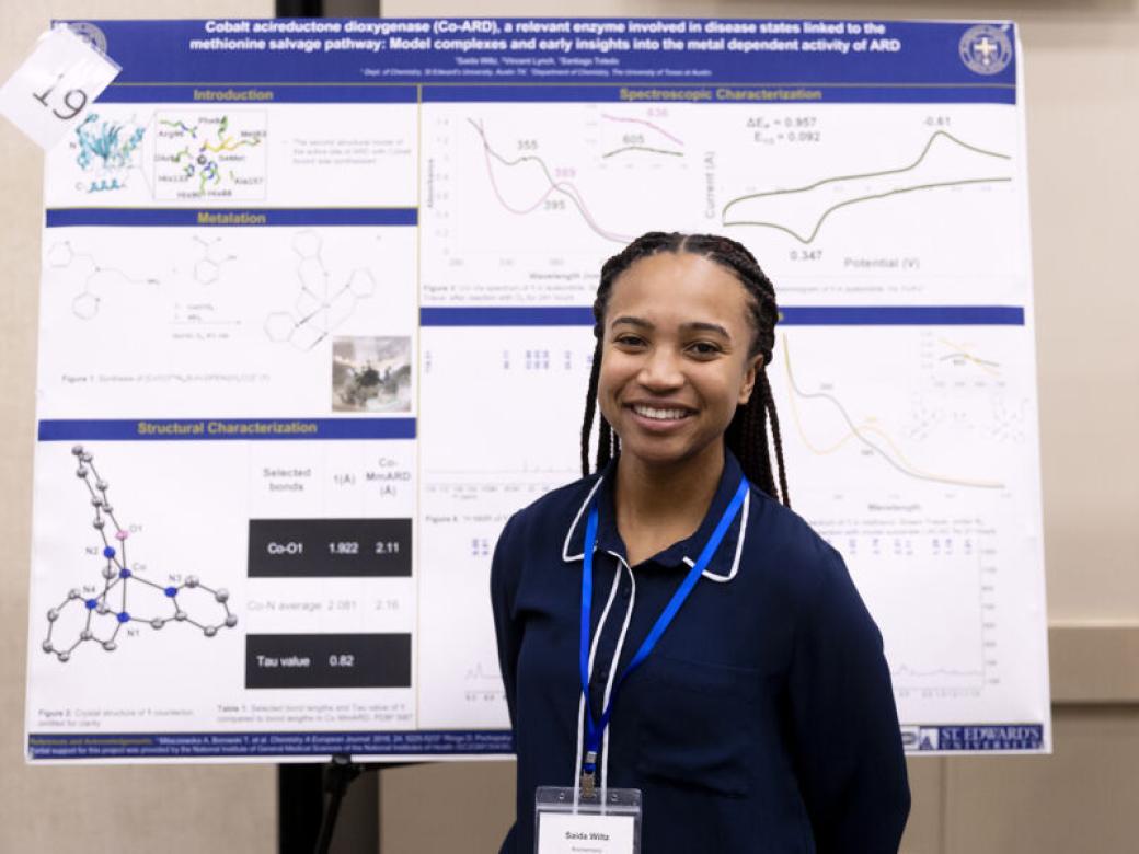 A biochemistry student stands by their research poster board.