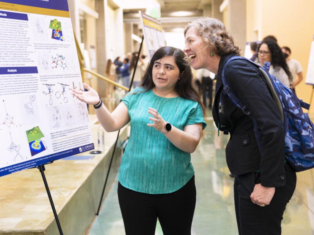 A student presents their research to a guest during the Lucian Symposium.