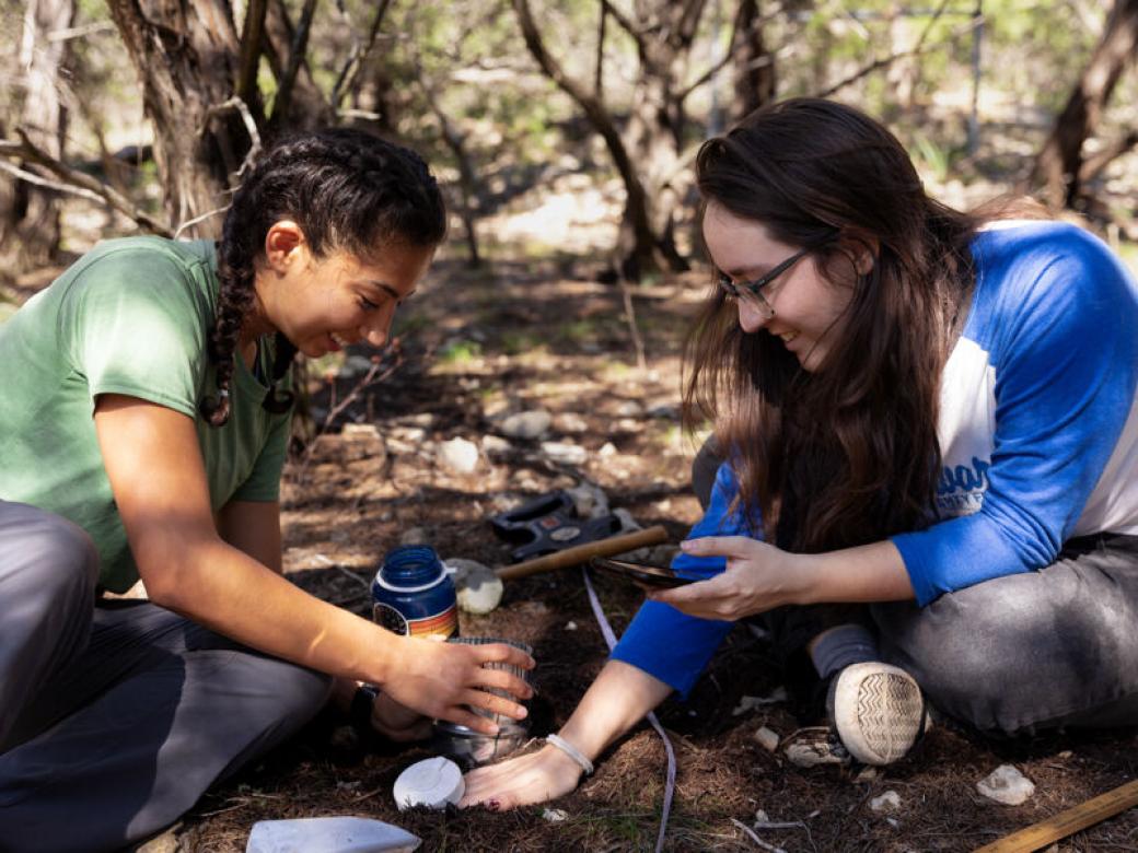 Two students sit on the ground and work on gathering data about the soil at Wild Basin.