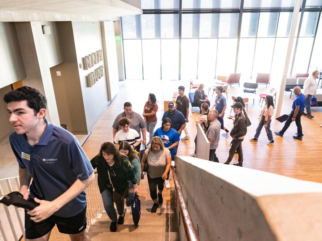 A student tour guide leads a tour of prospective students and their families up the stairs in Munday Library.