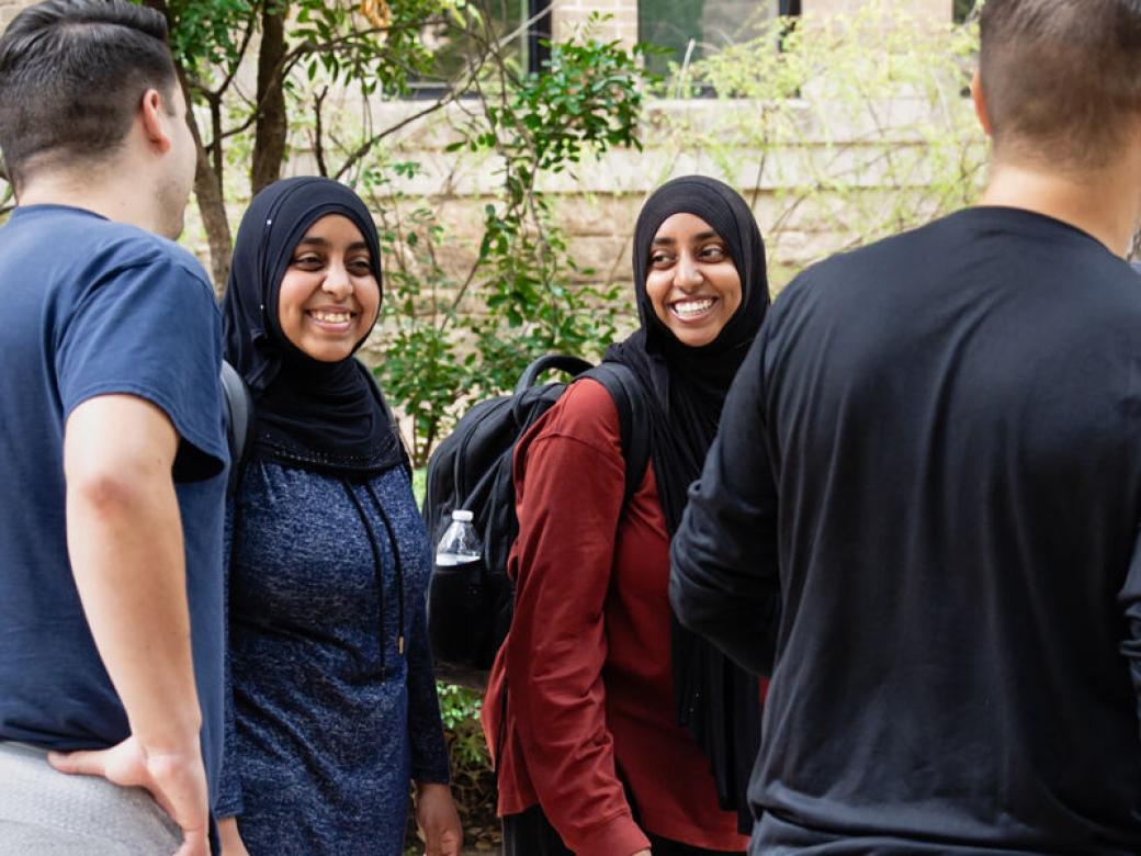 Two international students wearing hijabs smile and chat with other international students at an international student event.