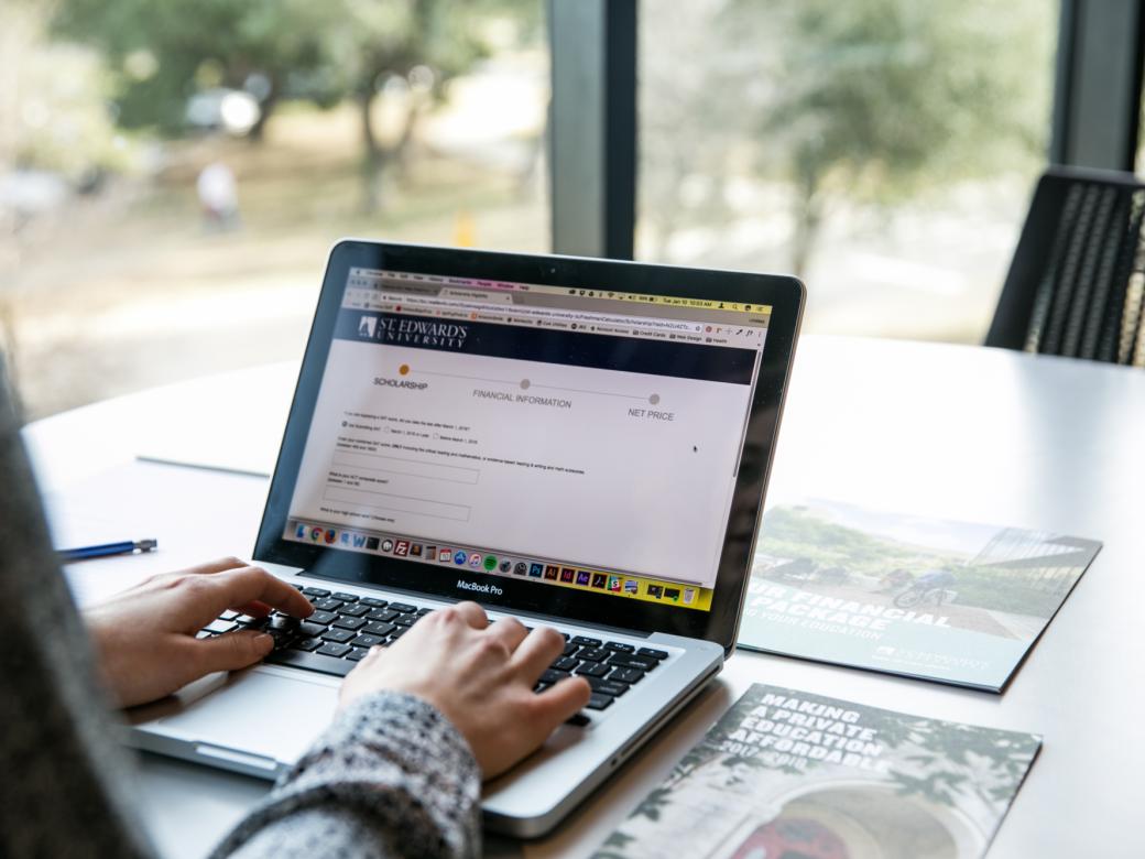 Hands type on a laptop. The screen shows information about scholarships and the net price calculator.