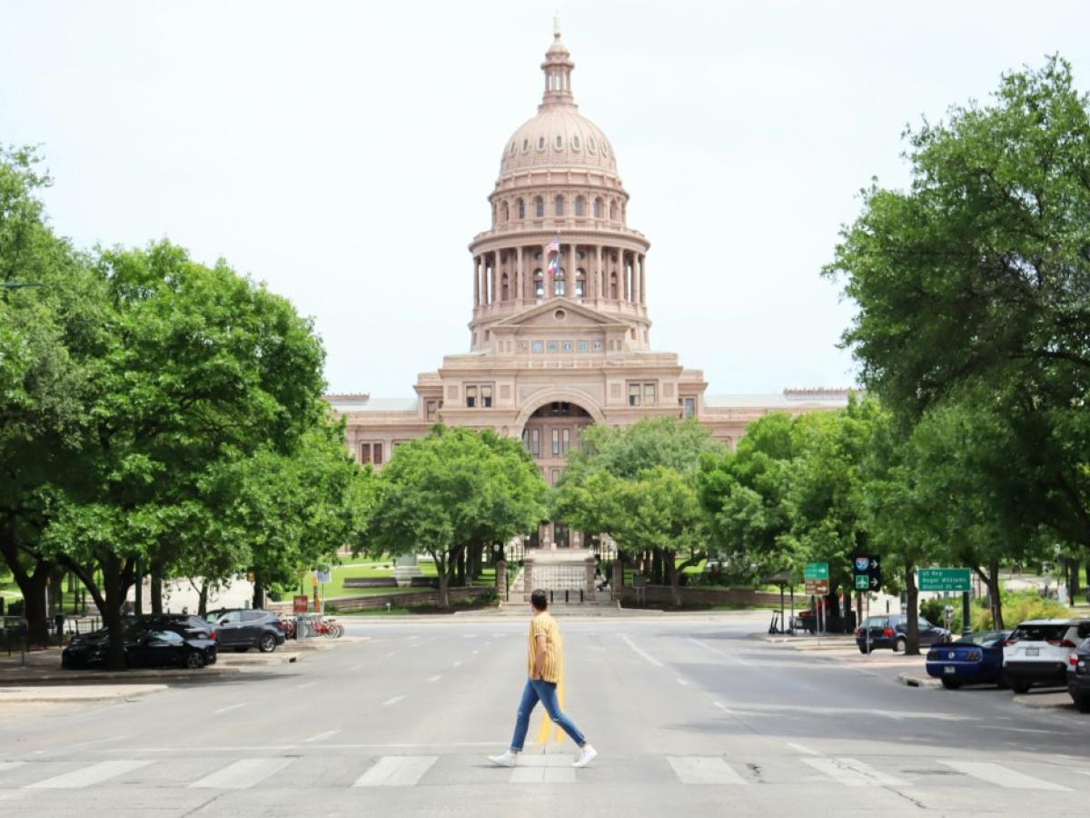 Person crossing a road with a capital building in the background.