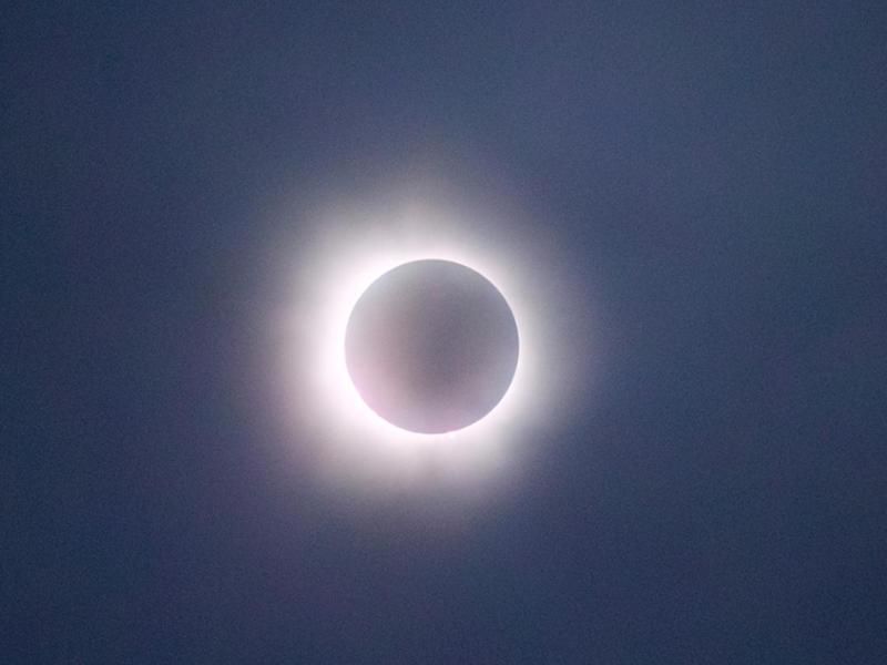 The image captures a solar eclipse in its totality phase, where the moon completely covers the sun, leaving only the bright corona visible as a glowing ring around the darkened disk. The sky appears dark, adding to the dramatic effect of the eclipse. The soft, glowing light of the corona creates a striking contrast against the shadowed moon, making this a captivating depiction of a natural celestial event.