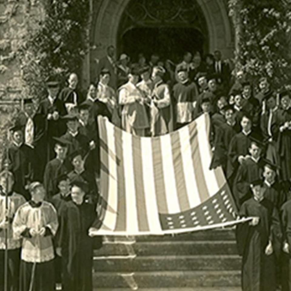 St. Edward's students and Holy Cross Brothers stand in front of the school with an American flag in the 1920s