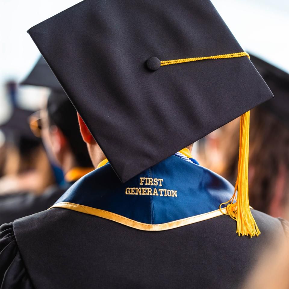 The back of a graduate is seen as they wear their cap, gown, and a stole that says first generation.