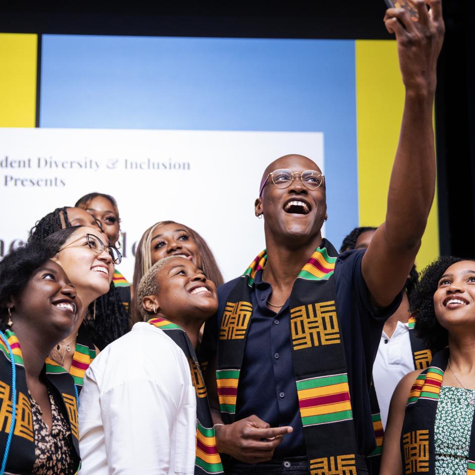 A group of graduates stand together wearing matching stoles and take a selfie during the Black Student Graduation Celebration.