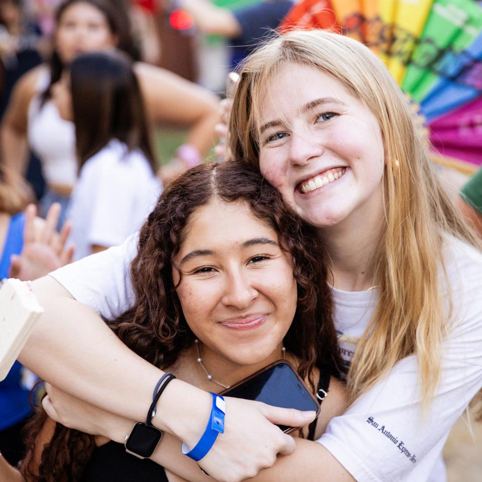 Two students embrace and smile at the camera during a university event.