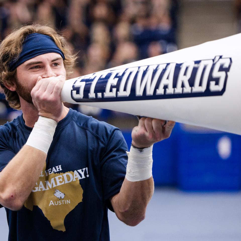 A cheerleader holds a megaphone that says St. Edward's and leads a cheer during a pep rally.