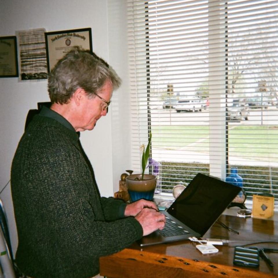 Professor Bill Quinn stands and types on his laptop in his office.