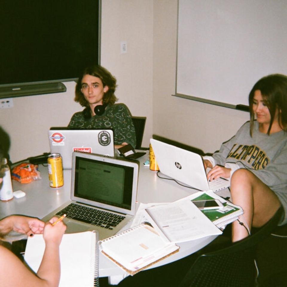 Students sit around a table with their laptops and study.