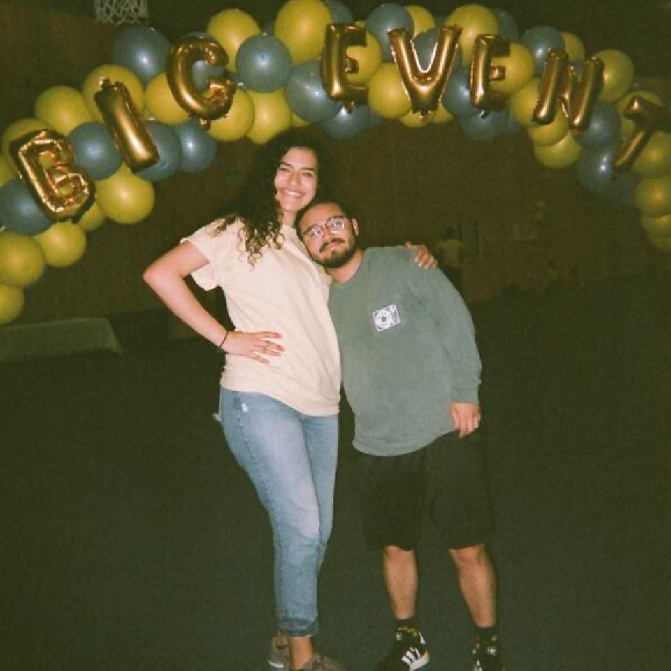 Two friends stand under a balloon arch that reads Big Event.