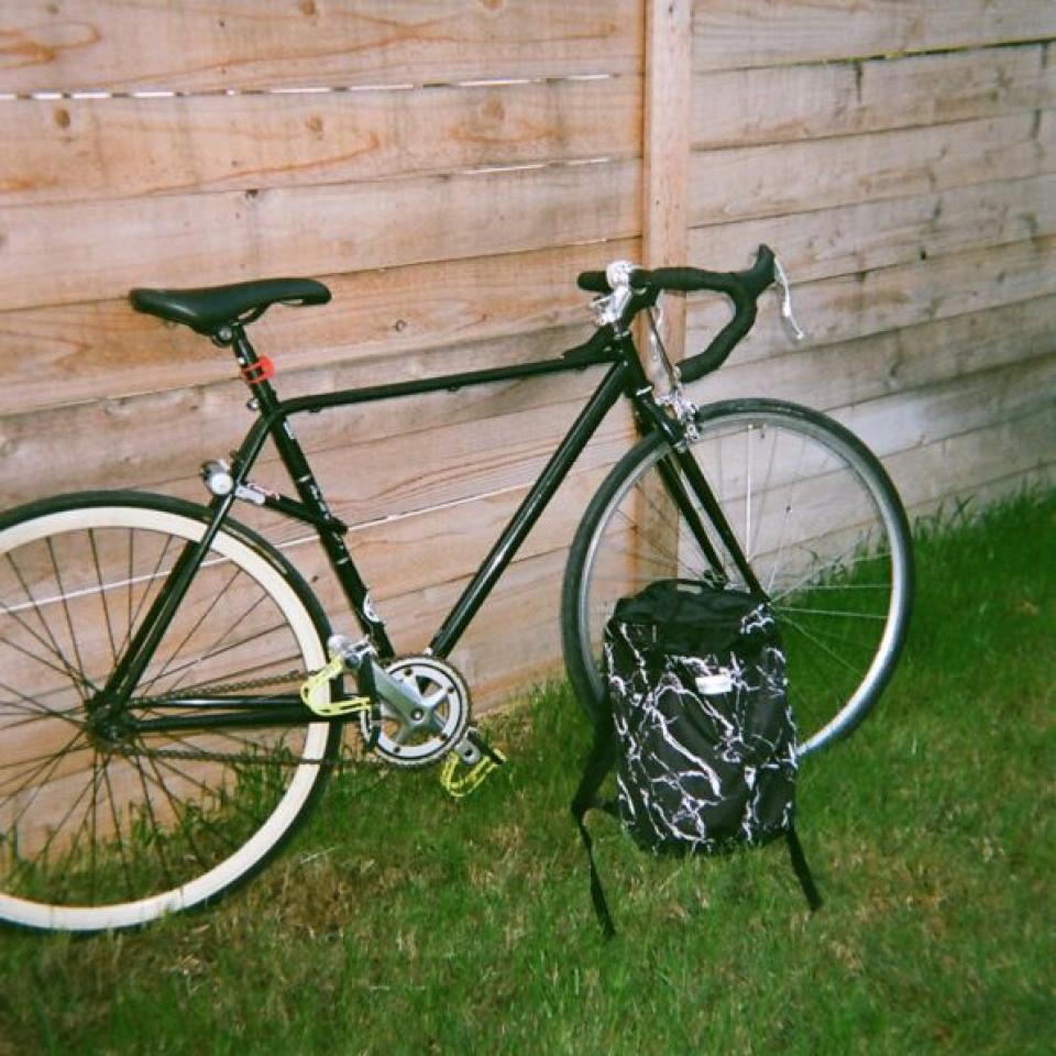 A bike and backpack rest against a fence.