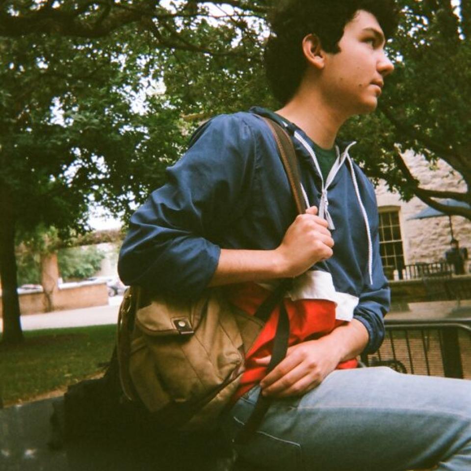 Alex Castillon sits on a patio table with his backpack.