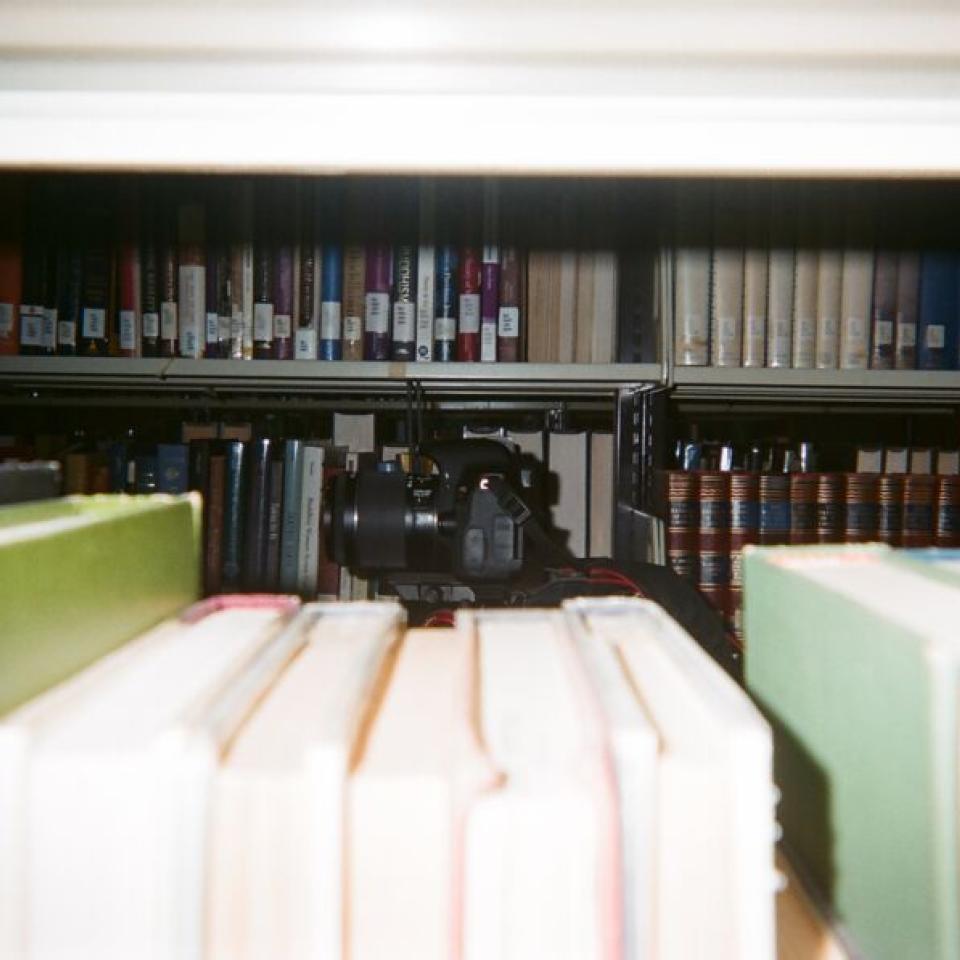 A camera is seen between a stacks of books in the library.