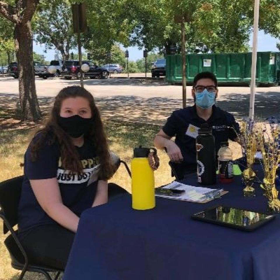 People wearing masks sit at a table outside.