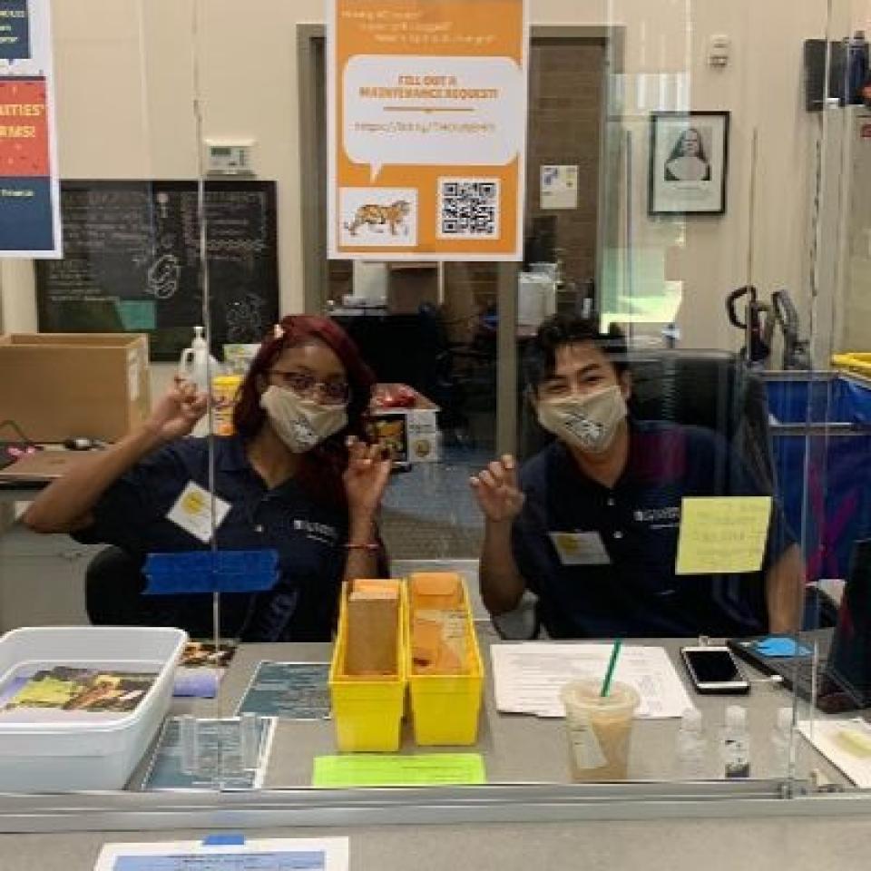 Two residence assistants wear face masks and make toppers up hand signs.