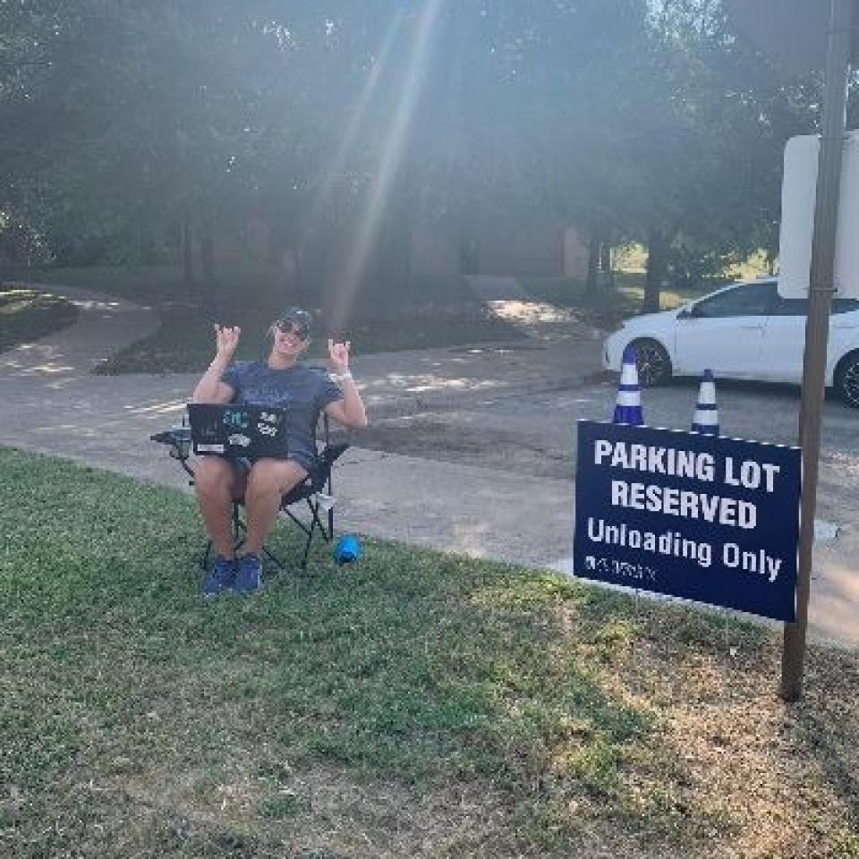 A person sits in a lawn chair by a parking lot reserved sign.