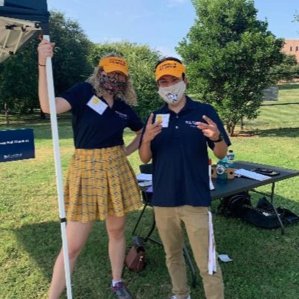 Two people wear blue and gold and face masks.