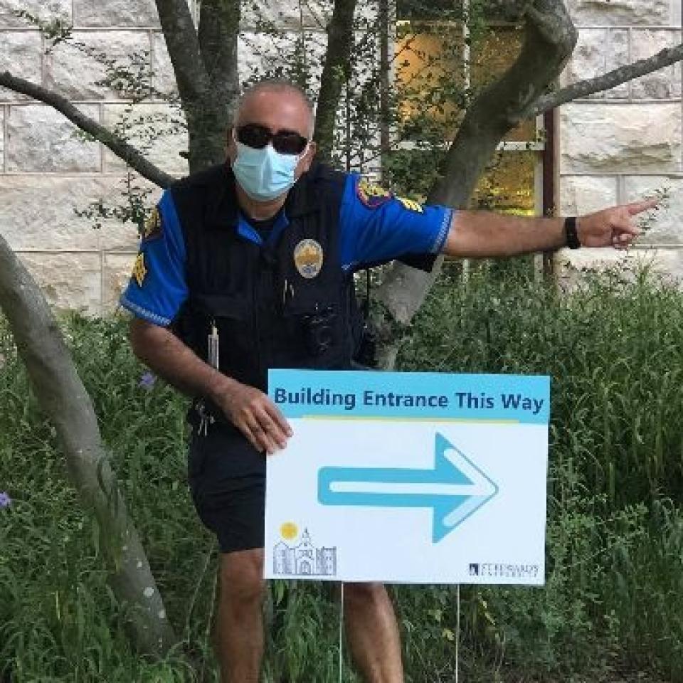 University Police Officer Nic Delgado wears a face masks and points to the building entrance.