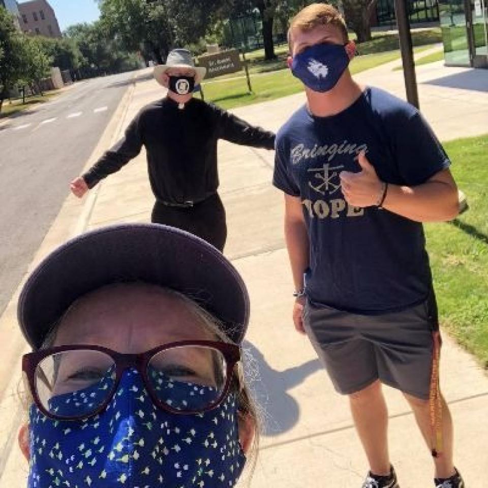 Lisa Kirkpatrick wears a face mask and takes a selfie with two people wearing face masks.