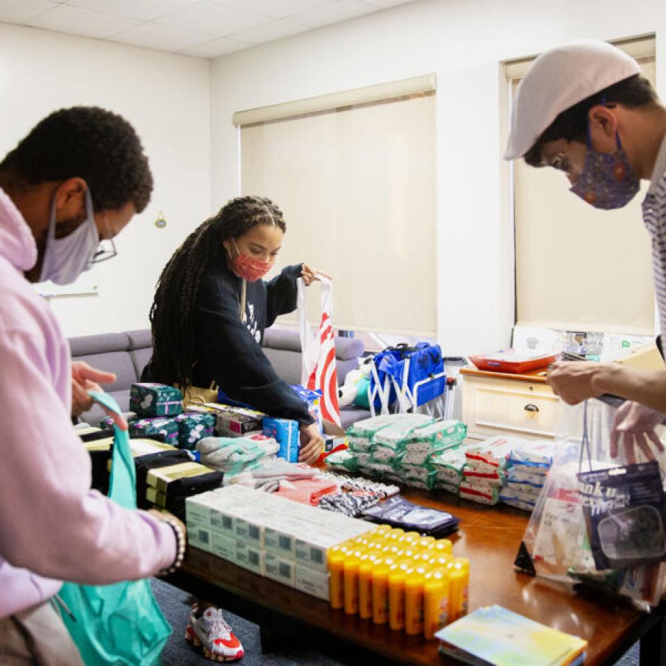 Taylor Huey, center, and two friends, all wearing face masks, pack wellness kits in a conference room.