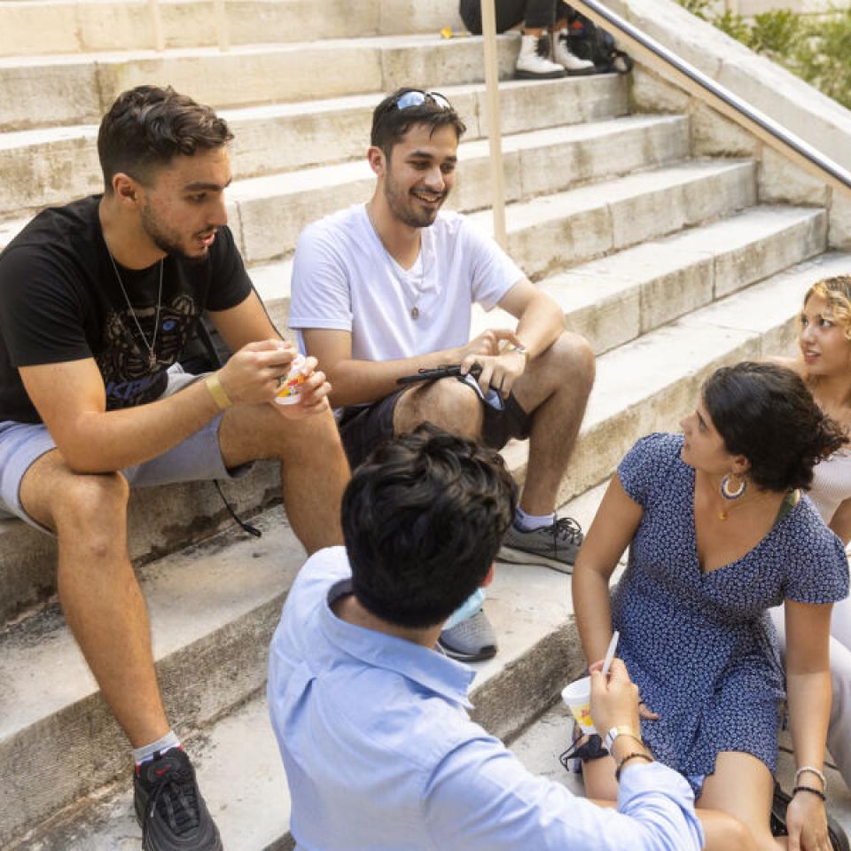 Students having a friendly discussion while sitting on the steps in front of Main Building.