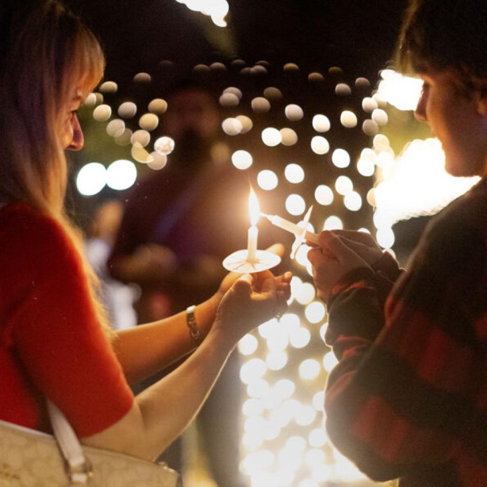 A student lighting another student's candle with their own