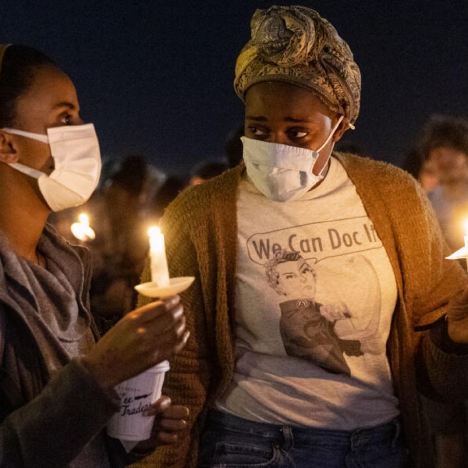 Two students wwearing medical masks, holding candles, one in a "We Can Do It" shirt