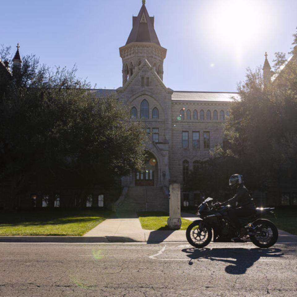 Sabur Khan riding his motorcycle in front of main building on campus 