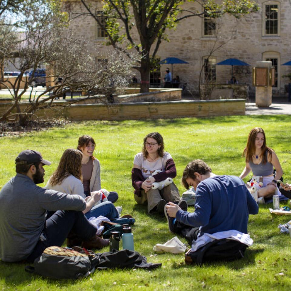 Students conversing while sitting in a circle on the grass on campus.