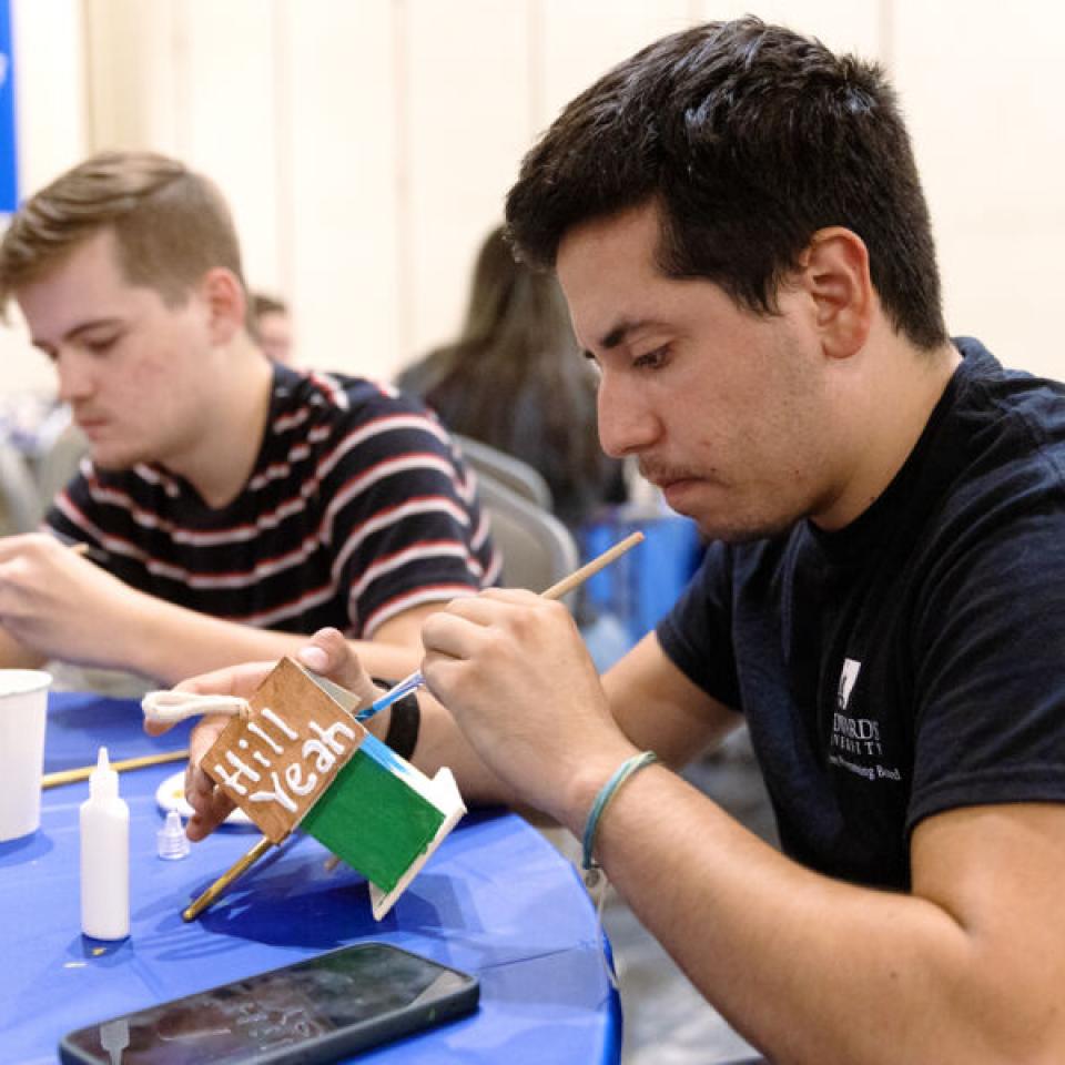 Ethan Tobias paints a birdhouse blue and green, with writing on the birdhouse roof reading "Hill Yeah" during an University Programming Board event he helped plan.