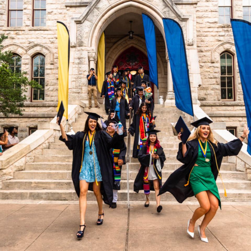 Graduates wearing caps and gowns walk down the steps of Main Building with their degrees during the Legacy Walk.