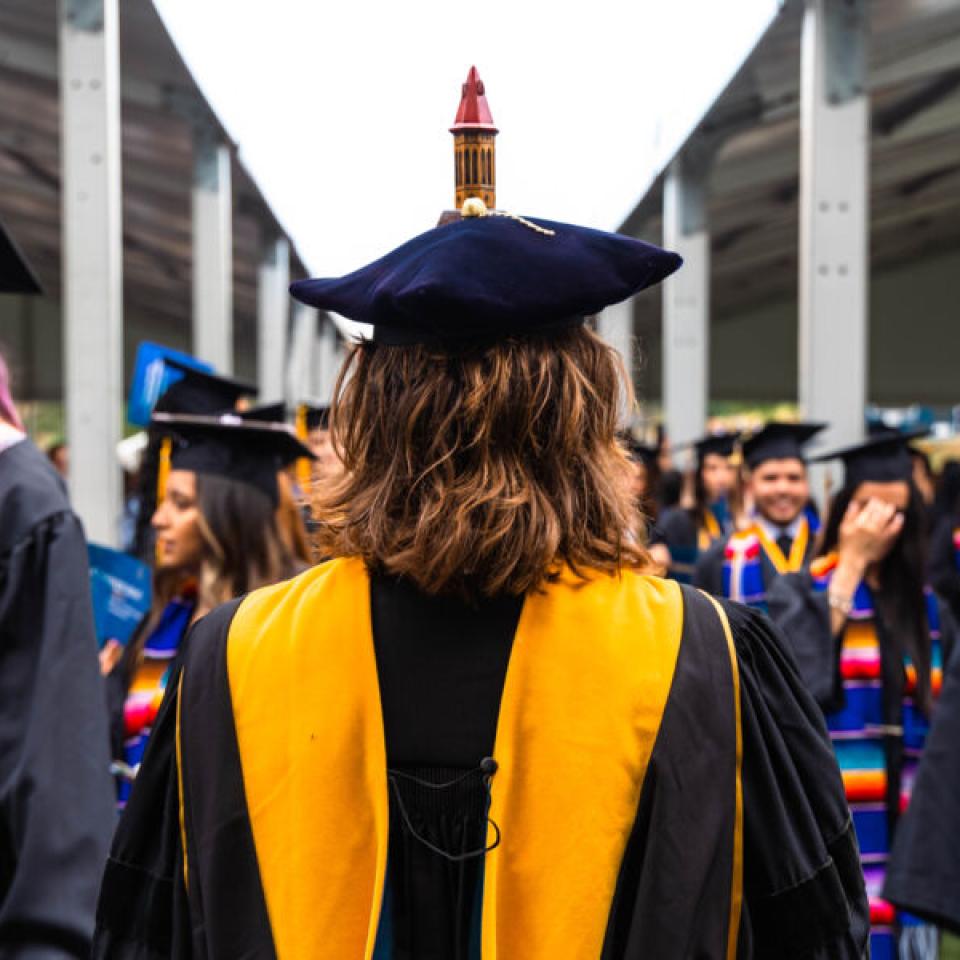 Graduating senior walking toward fellow graduates at commencement.