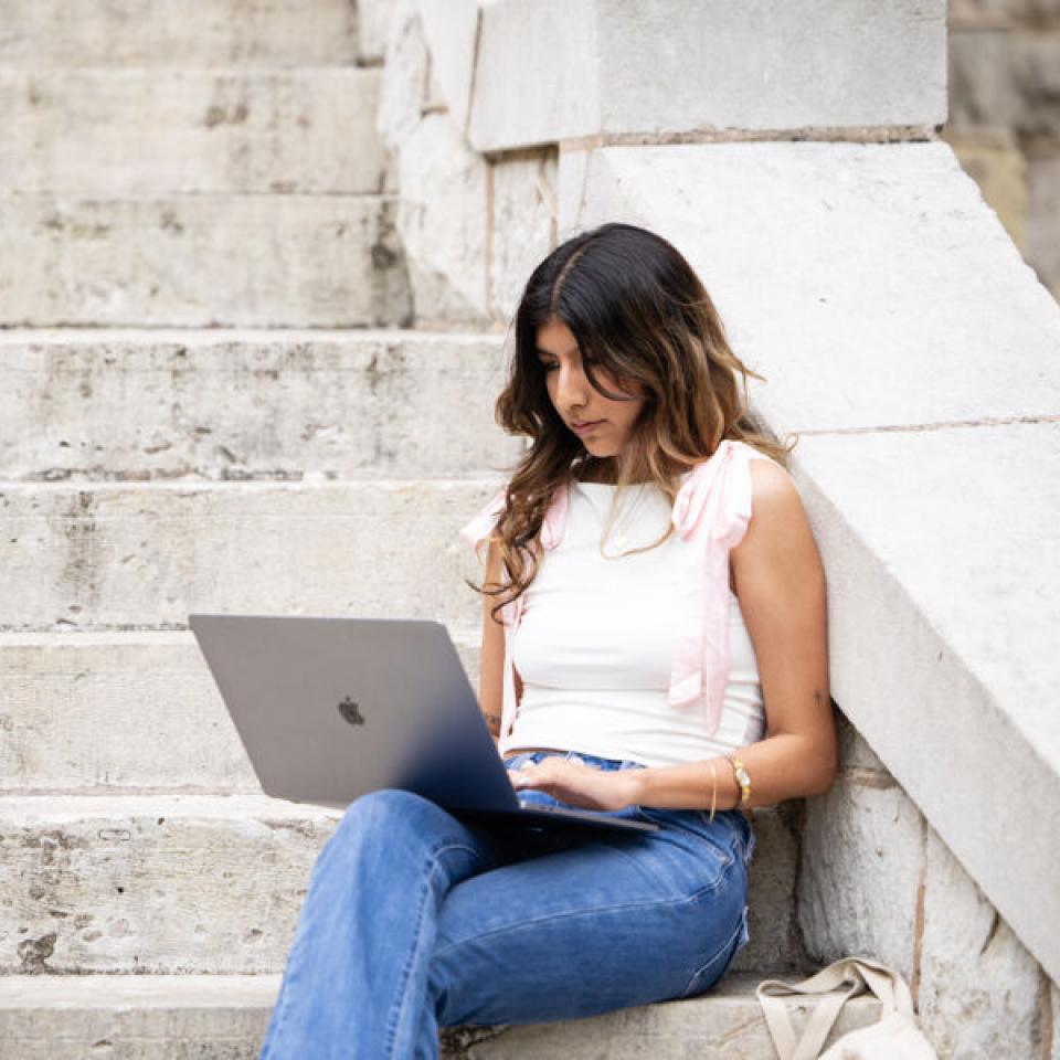 Student studying on her laptop on the front steps of Main Building.