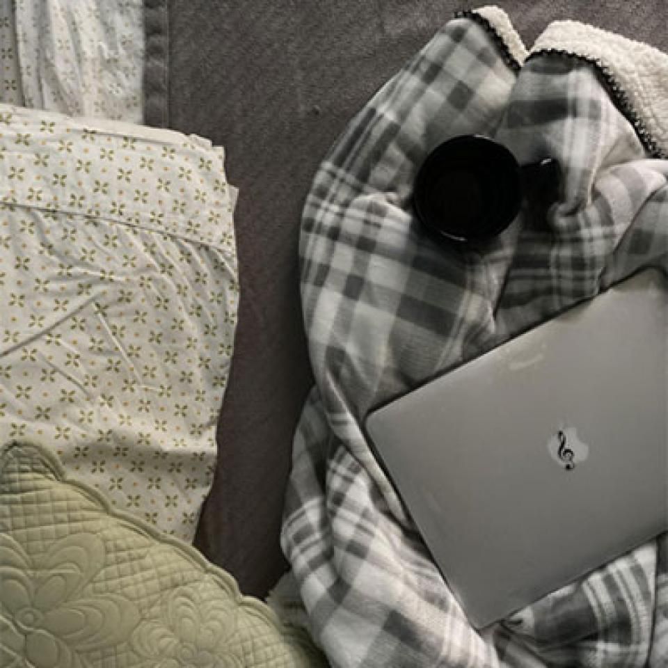 A laptop on a blanket and pillows.