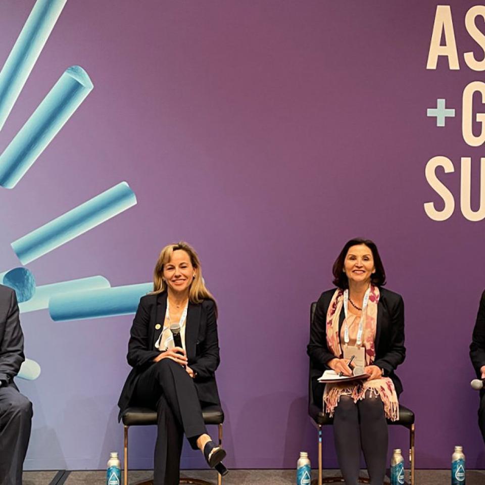 The image shows four panelists seated on a stage at the ASU+GSV Summit. The background features the event's logo on a purple backdrop with blue cylindrical shapes. The panelists, three women and one man, are dressed in business attire and appear engaged and ready to speak. They have microphones and notes, indicating a formal discussion or presentation. The setting suggests a professional conference focused on education, technology, or innovation.