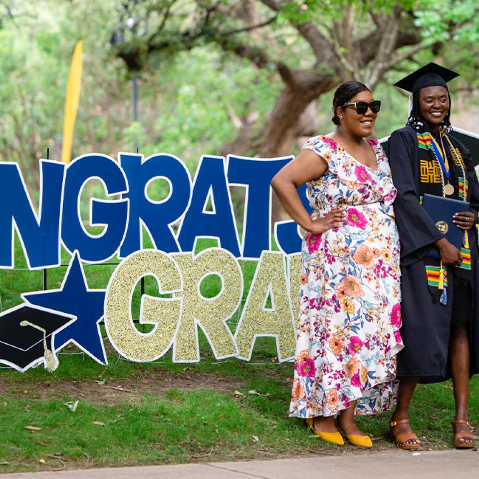 Graduate posing near celebration signs at Spring Commencement 2023