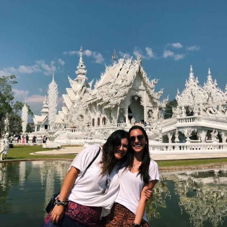 Aida Domingo and a friend stand in front of a pond that is in front of a temple.