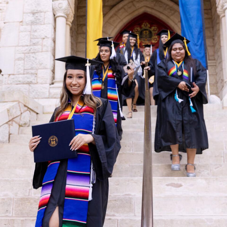 students in camp and gowns walking out of the iconic red doors