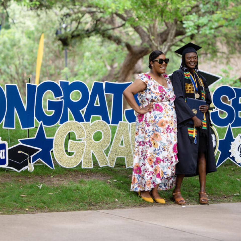 graduate posing with relative near graduate signs