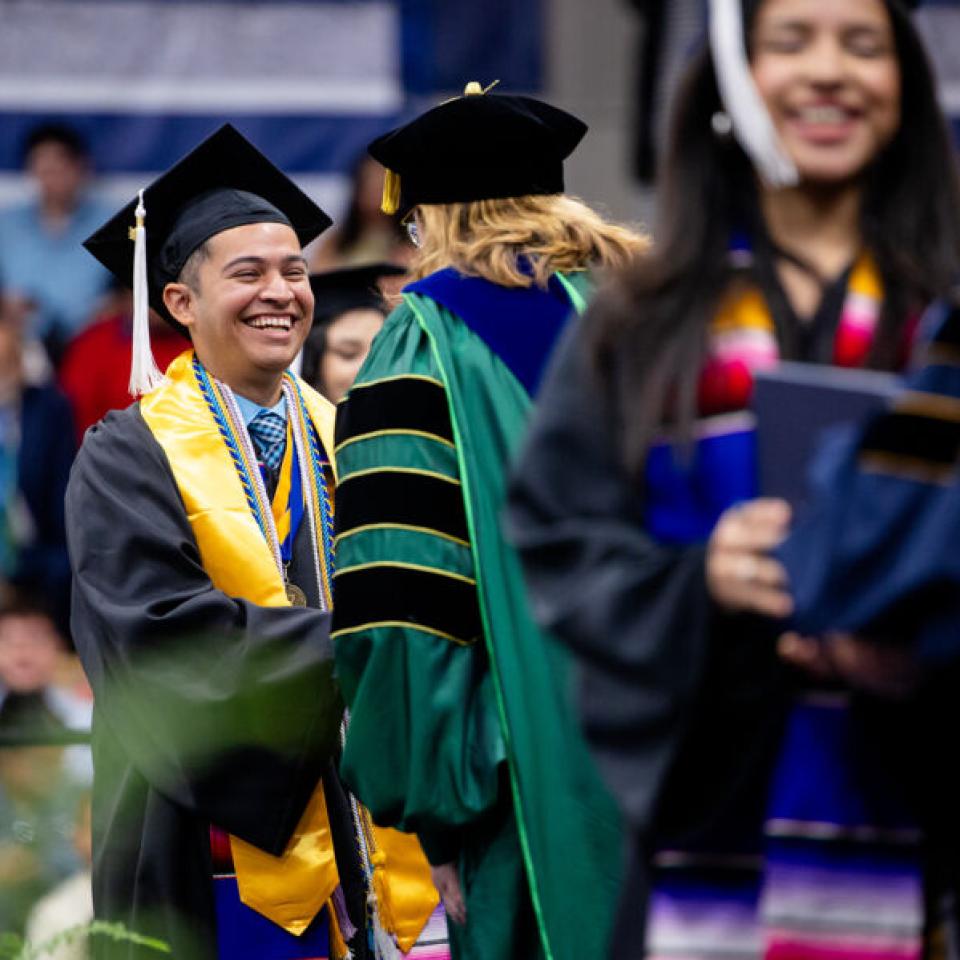 A graduates receives his diploma on stage at commencement at St. Edward's University