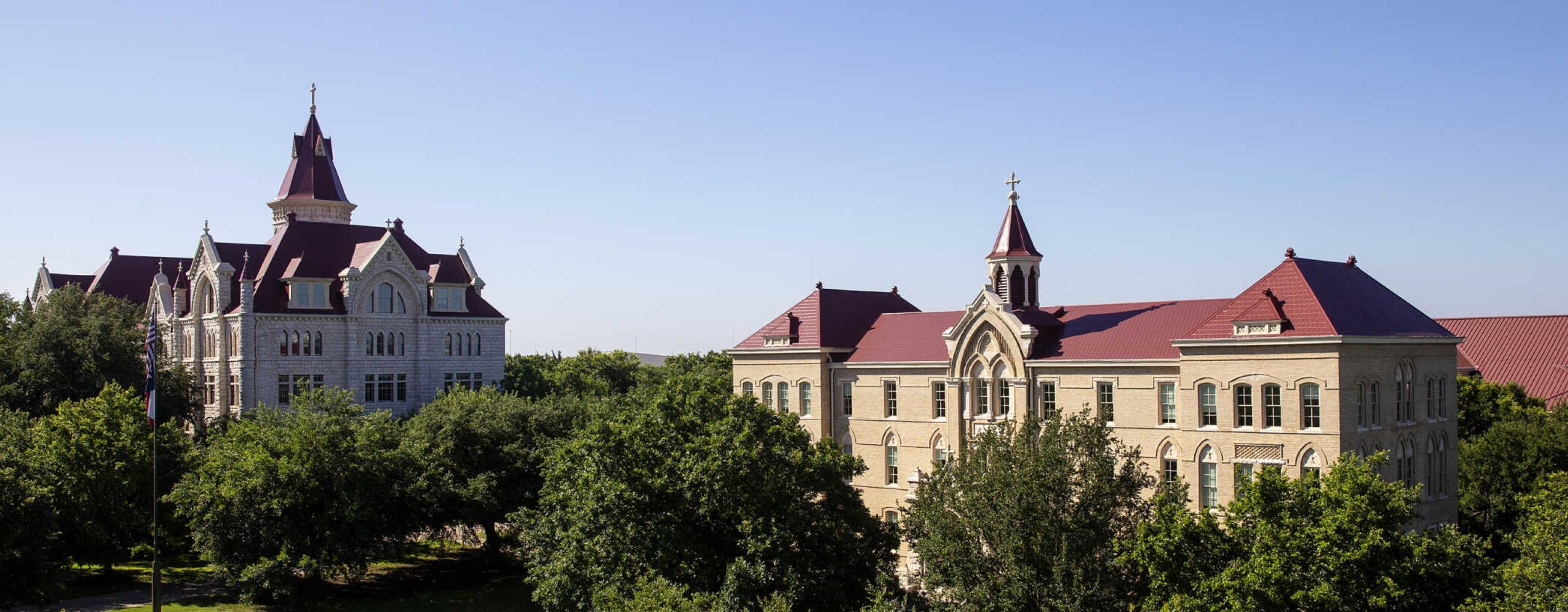 An aerial view of Main Building and Holy Cross Hall, surrounded by lush trees and green grass.