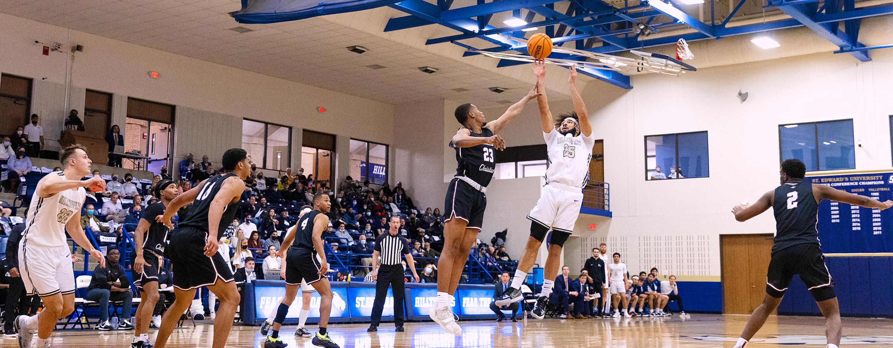 A St. Edward's men's basketball player shoots the ball as teammates and the visiting team look on.