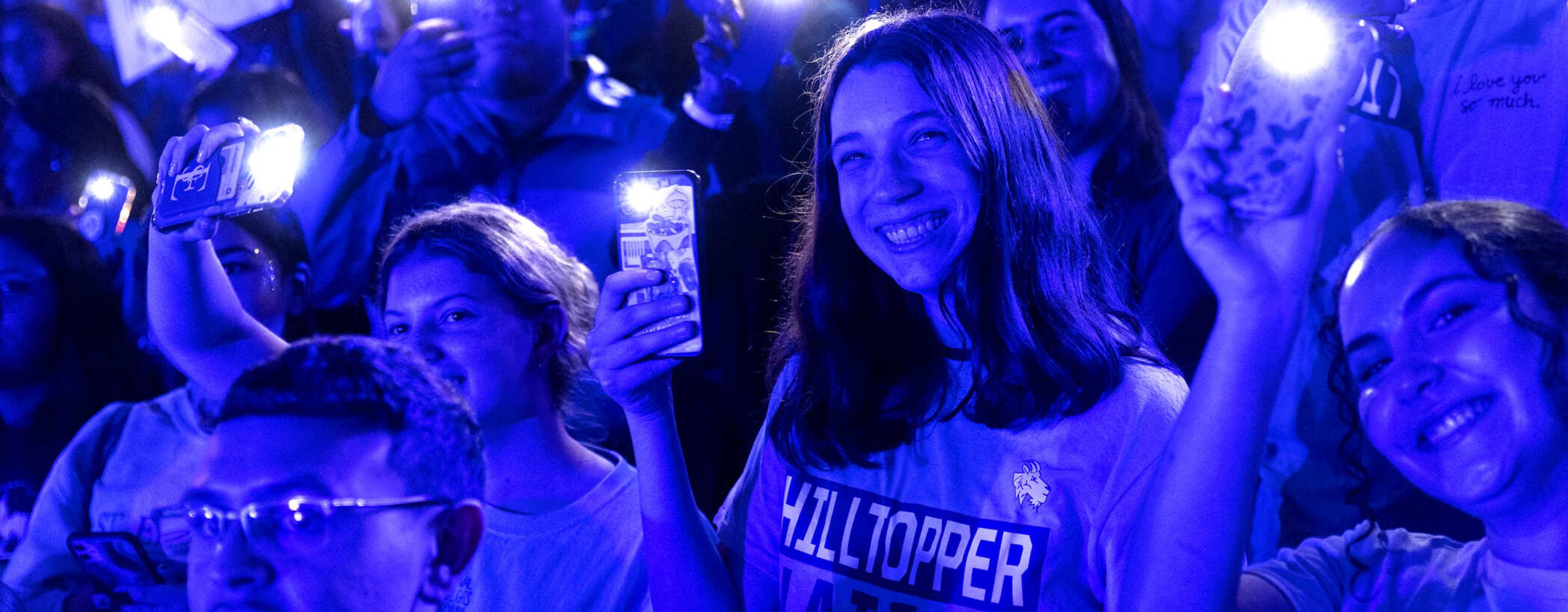 Students are illuminated by blue light and their cell phone flashlights during a pep rally.