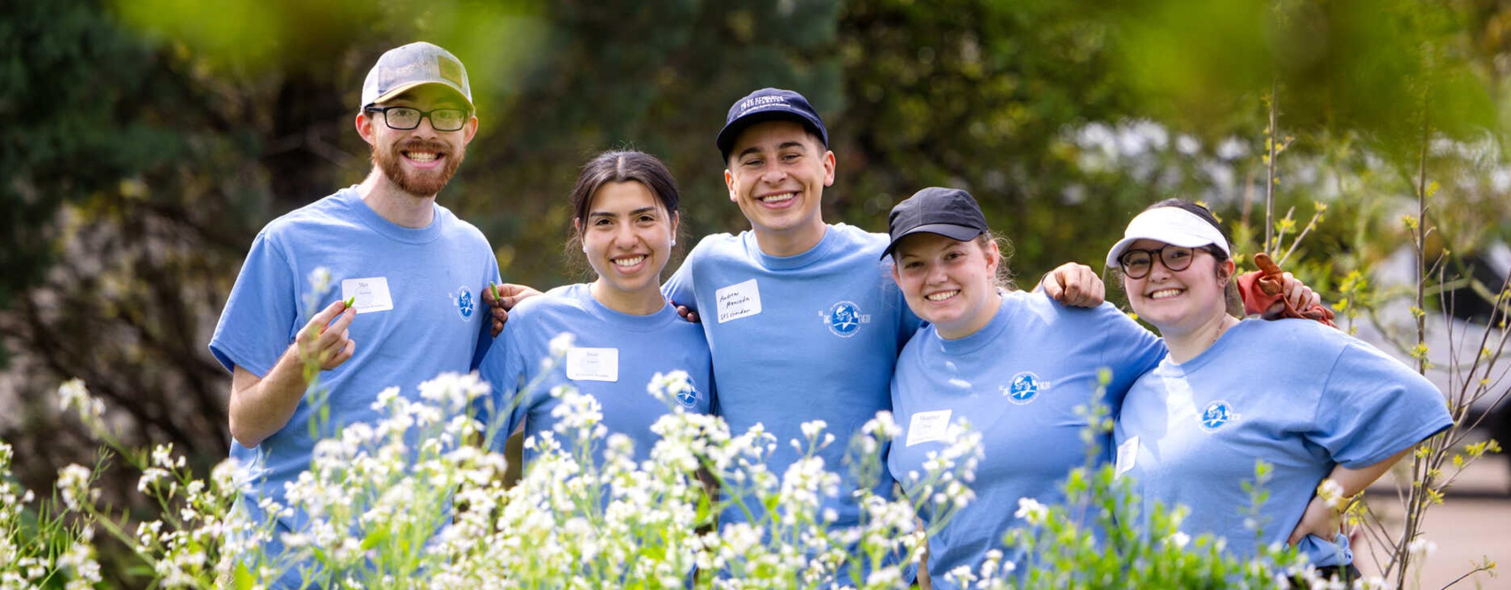 Five students wearing matching blue Big Event shirts are framed by foliage.